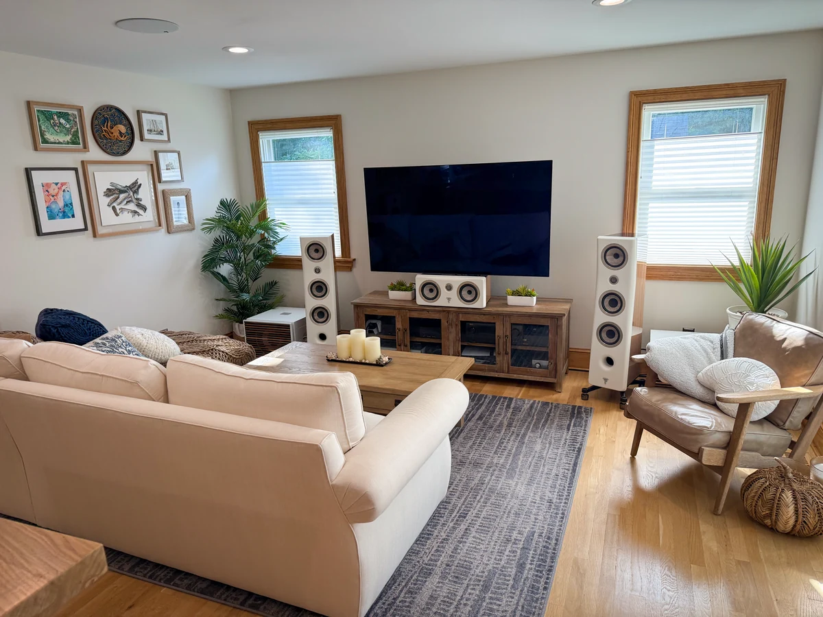 Wide view of the listening room, with cream sectional, white Focal speakers, oak console, navy rug and leather chair